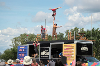 Acrobats balance on top of a food truck.